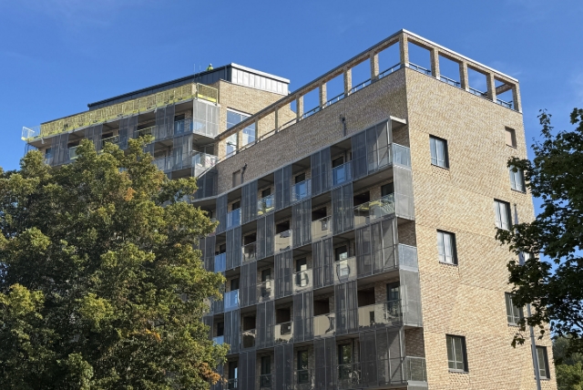 Hus under uppförande, med gul tegelfasad och inglasade partier.