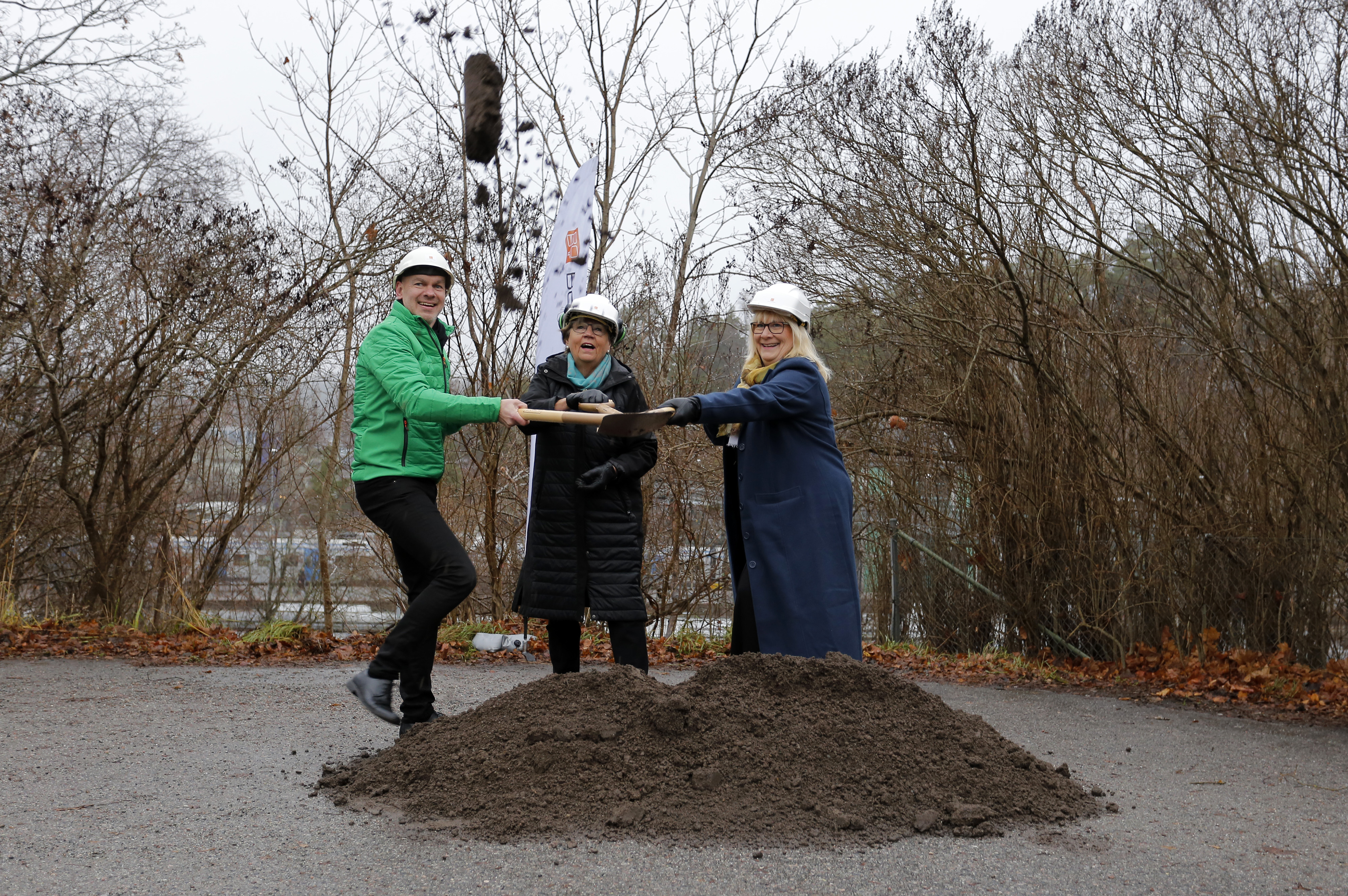 Tre personer kastar upp jord från en jordhög med en gemensam spade.