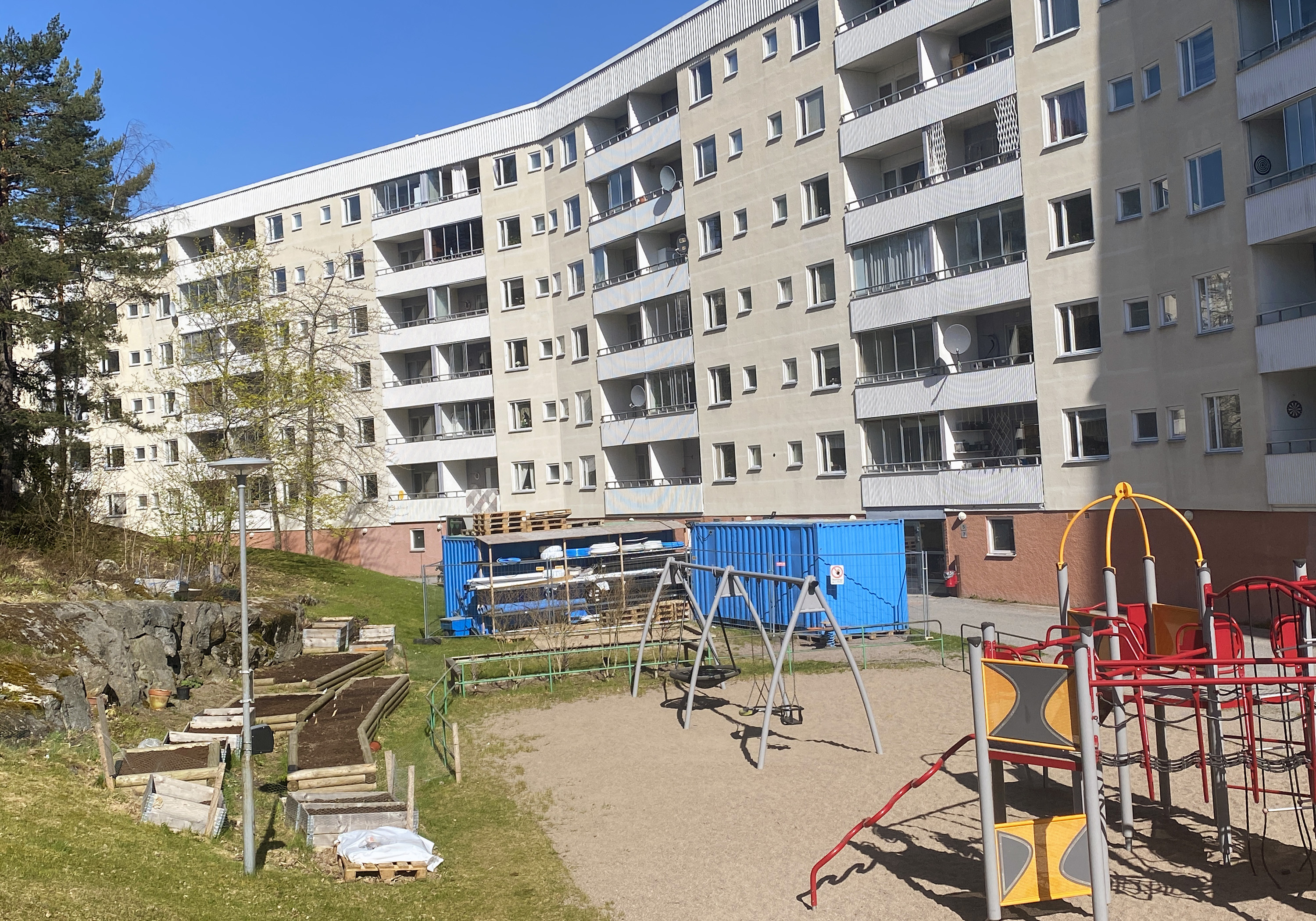 Ljust flerbostadshus i Storvreten med containrar utanför entrén.