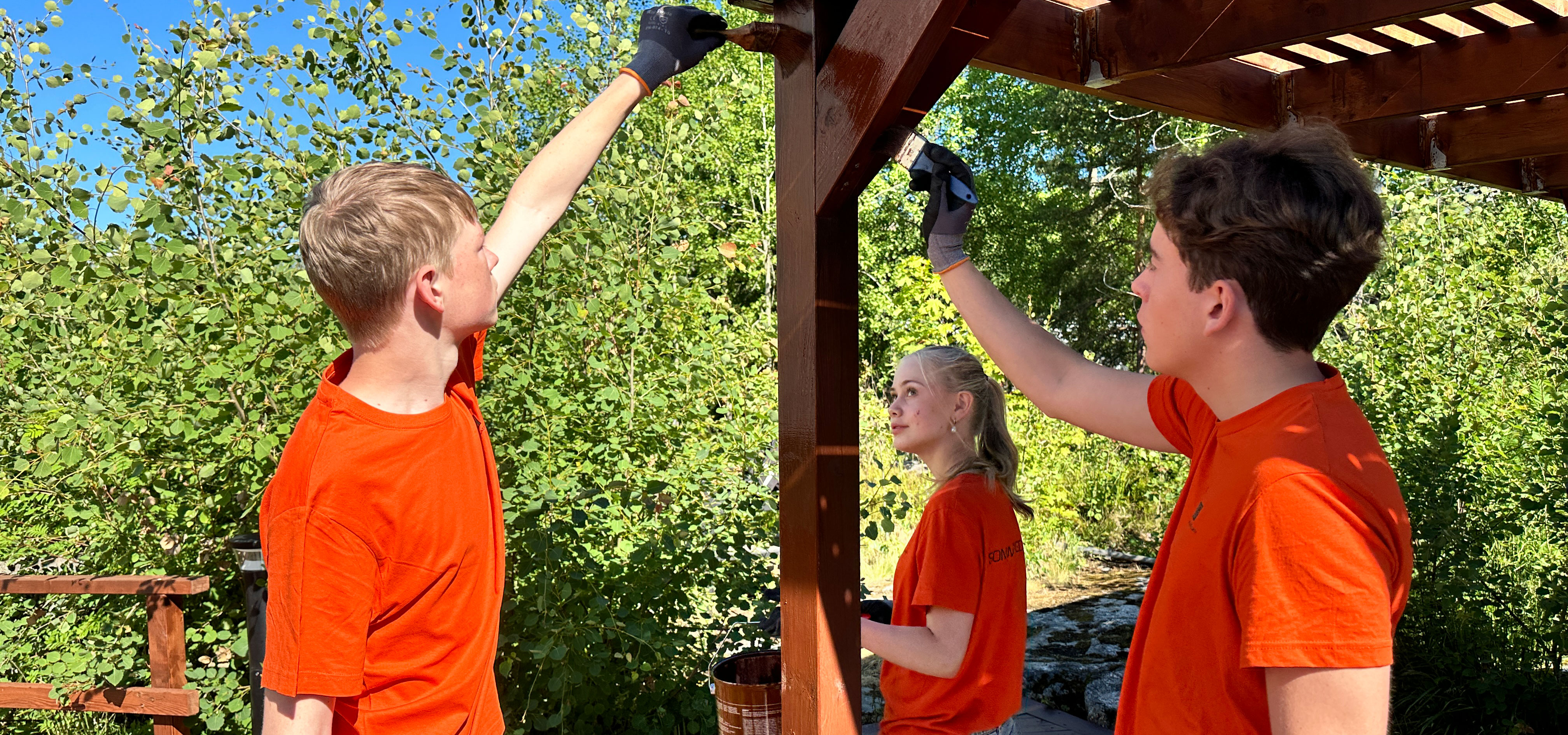 Tre ungdomare i orange t-shirt oljar in en pergola