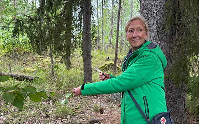 En kvinna i grön jacka klipper ett invigningsband i en skogsglänta