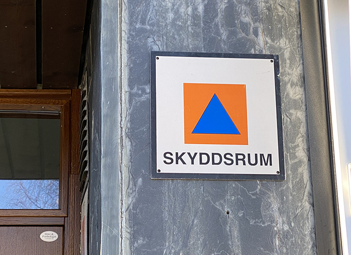 Skylt vid entré som visar symbolen för skyddsrum
