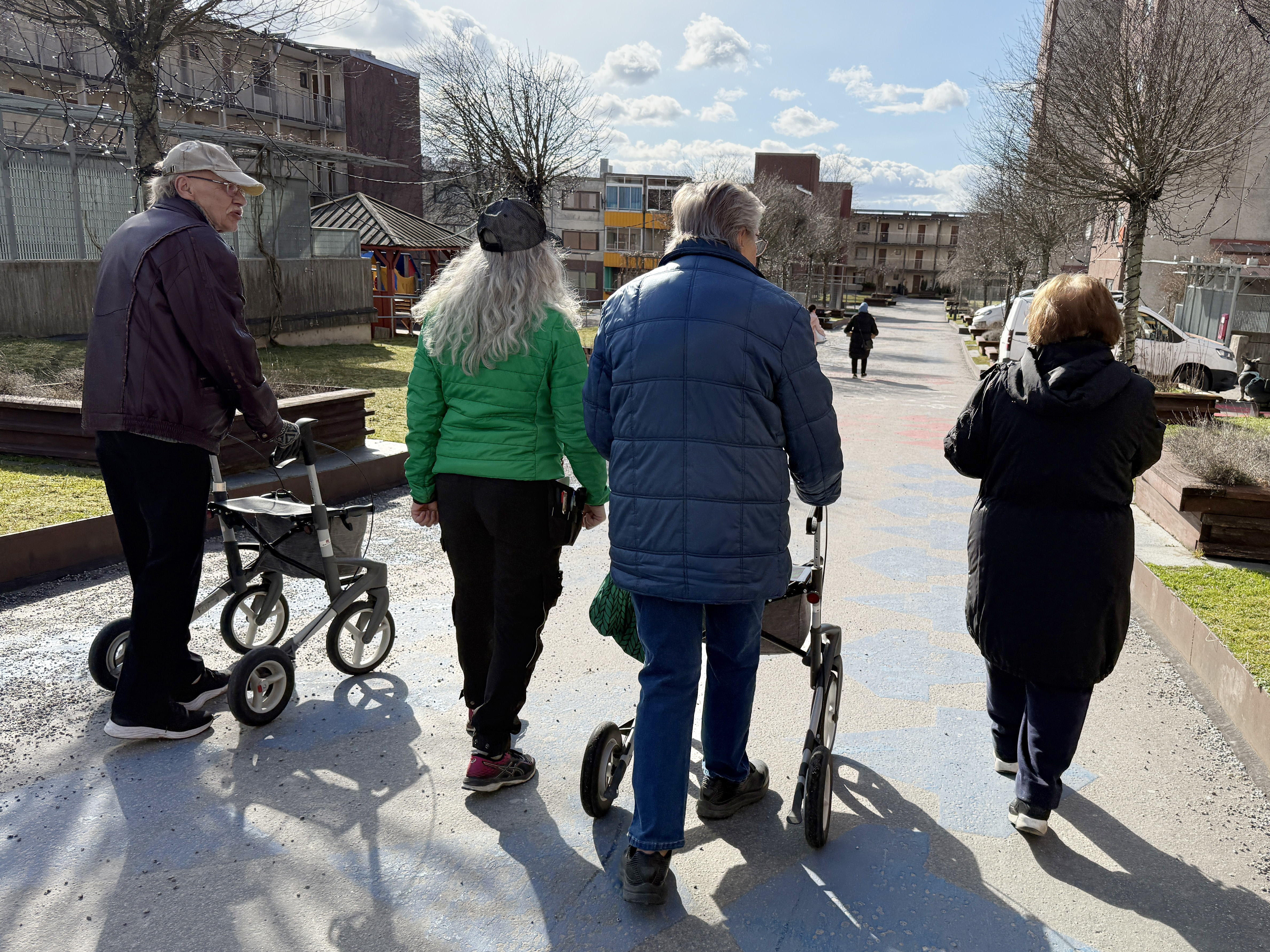 Fyra personer går bredvid varandra i ett soligt bostadsområde.