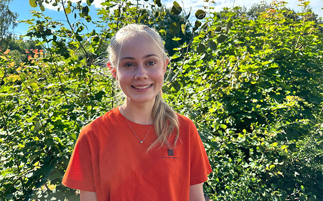 En tjej i orange t-shirt står framför ett träd