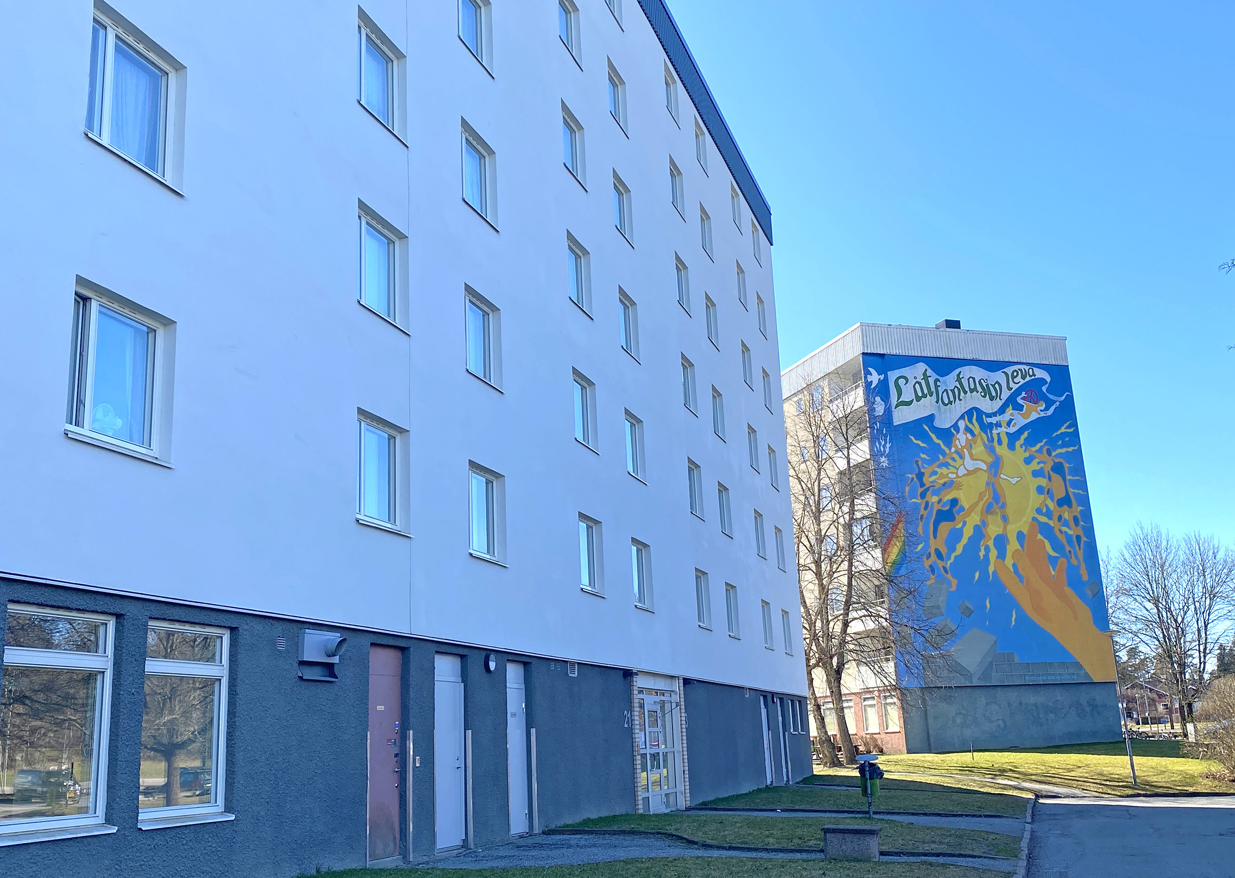 Två flervåningshus, ett vitt i förgrunden och ett med färgglad målning på gaveln i bakgrunden