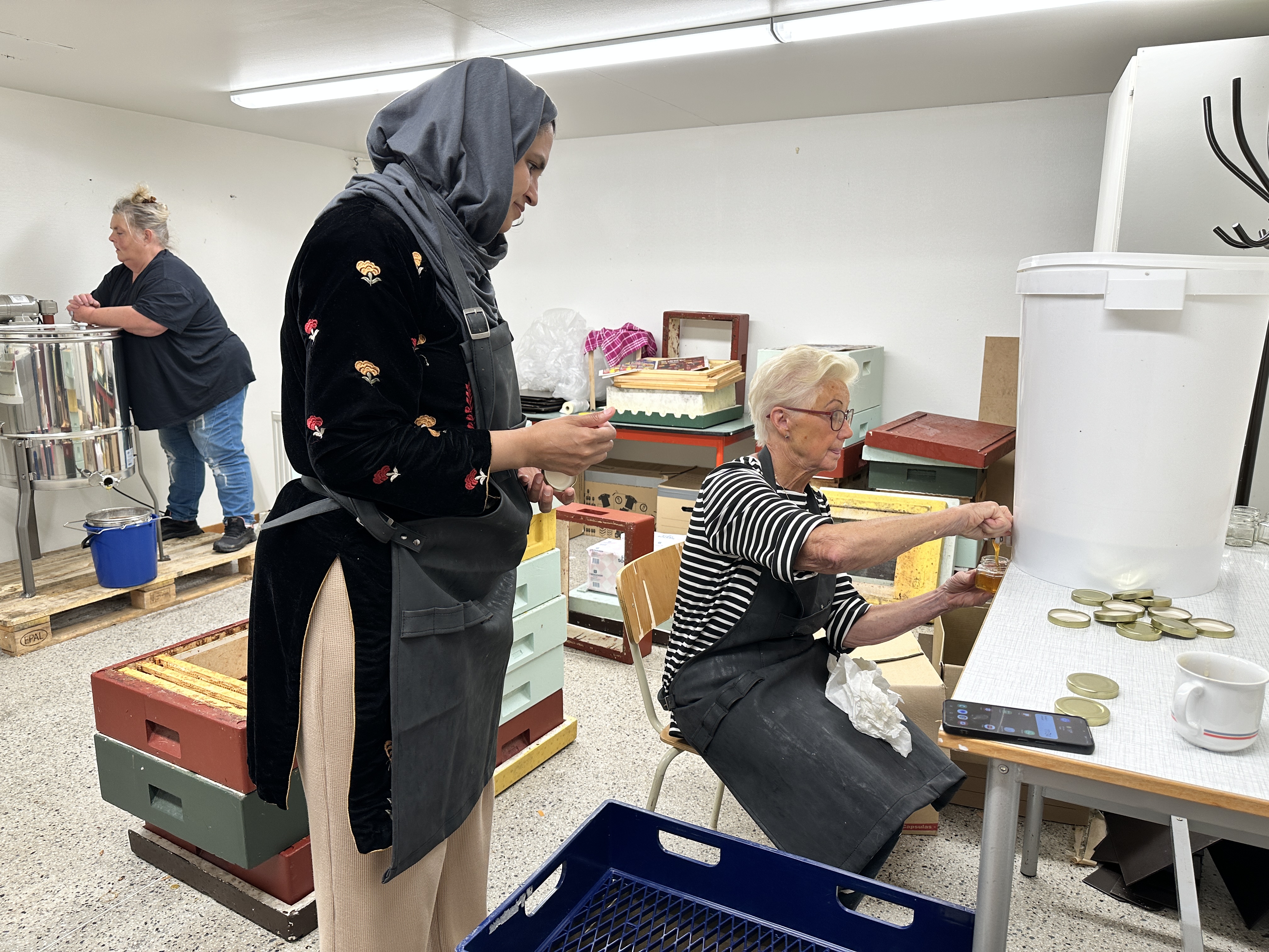 Tre kvinnor slungar honung och tappar på burkar