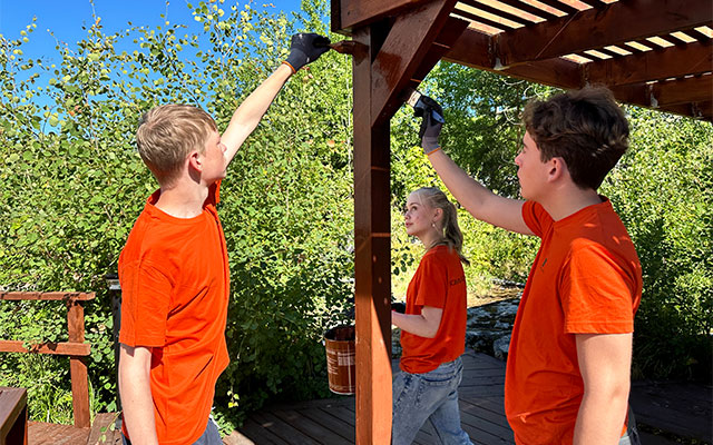 Tre ungdomare i orange t-shirt oljar in en pergola