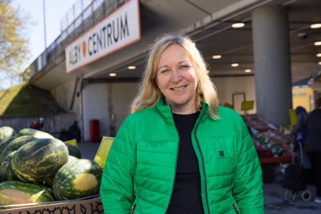 En blond kvinna i grön jacka står framför ett bord med vattenmeloner