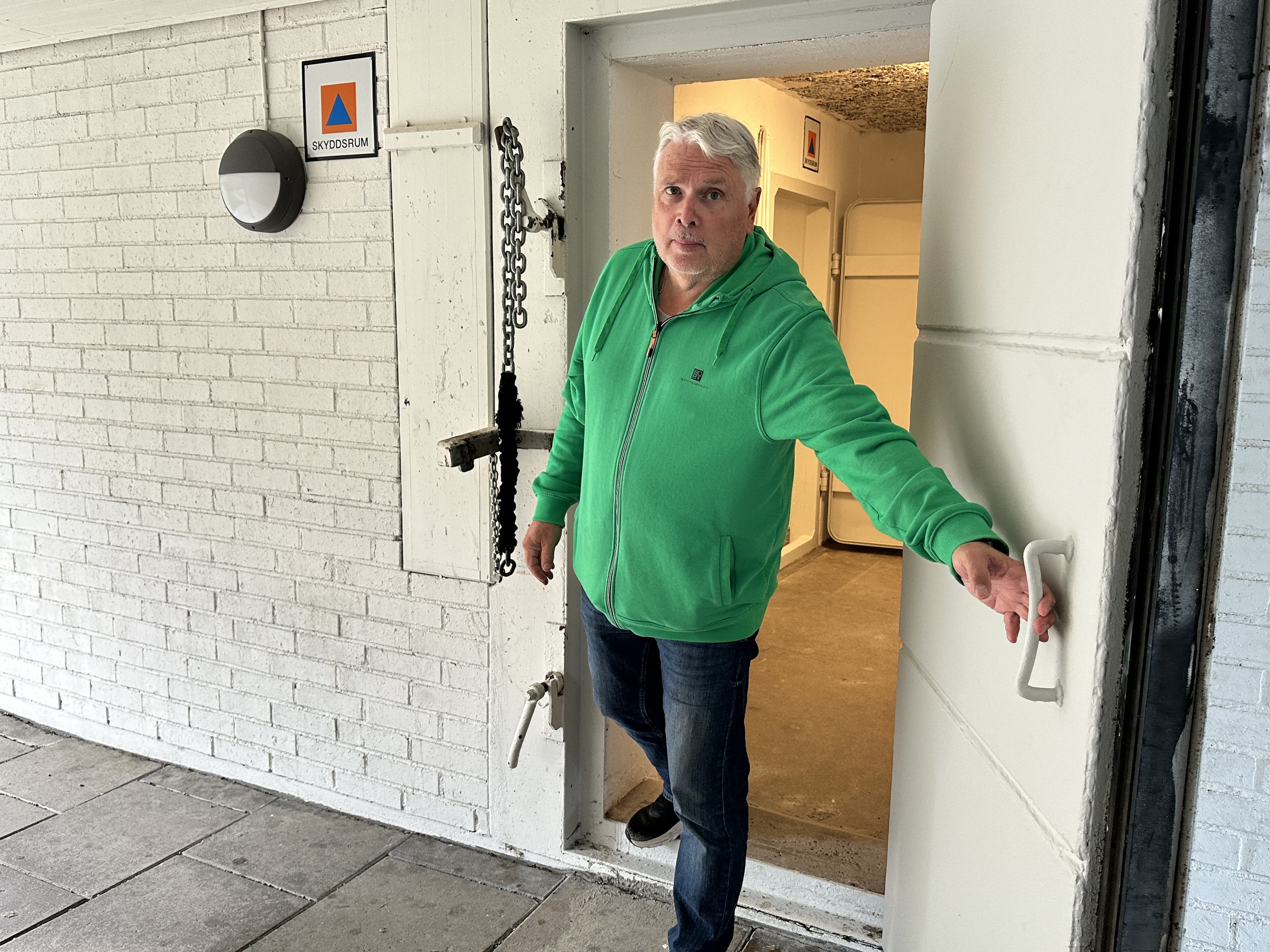 En man i grön tröja håller upp dörren till ett skyddsrum.
