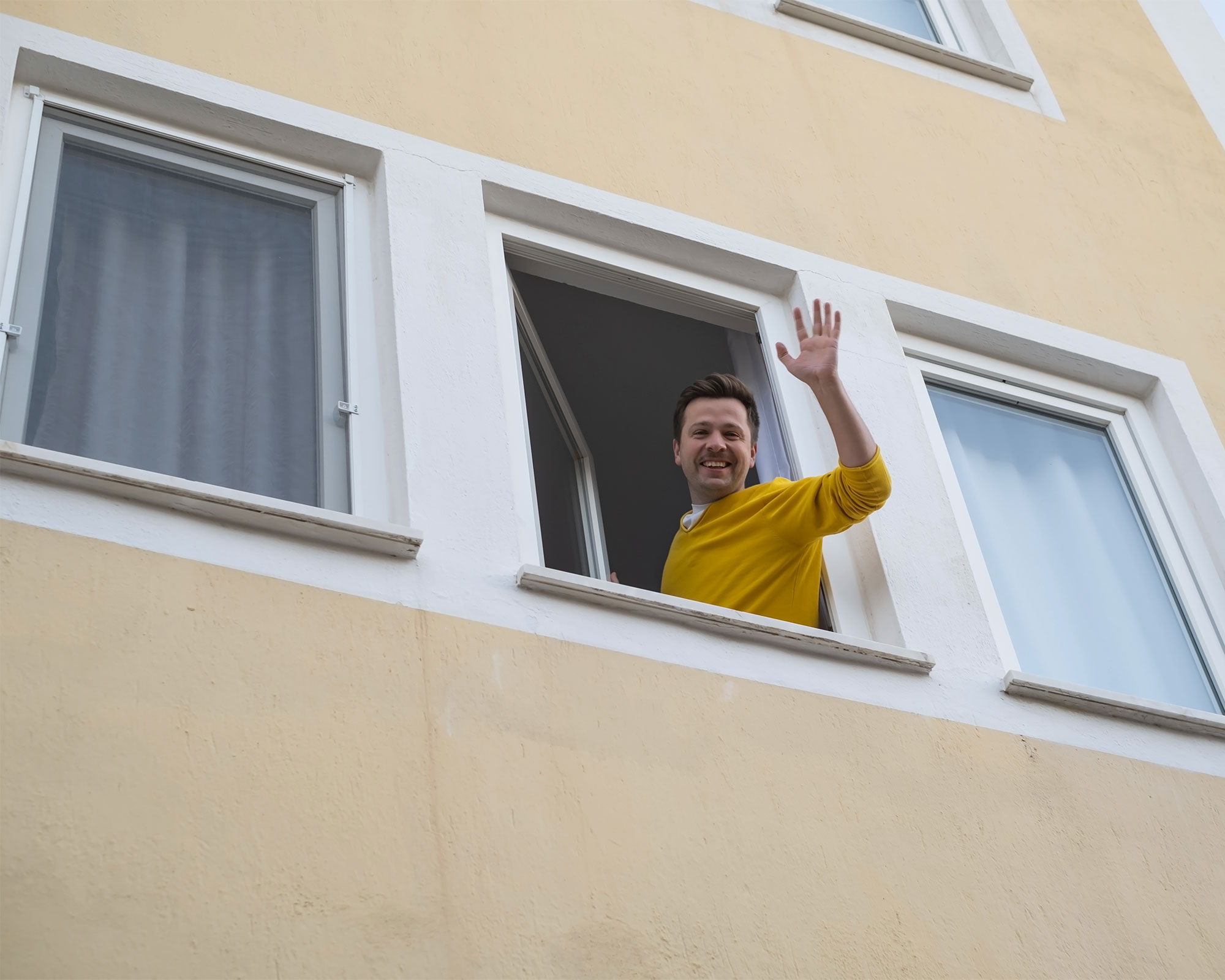Man står vid ett öppet fönster och vinkar till någon nedanför