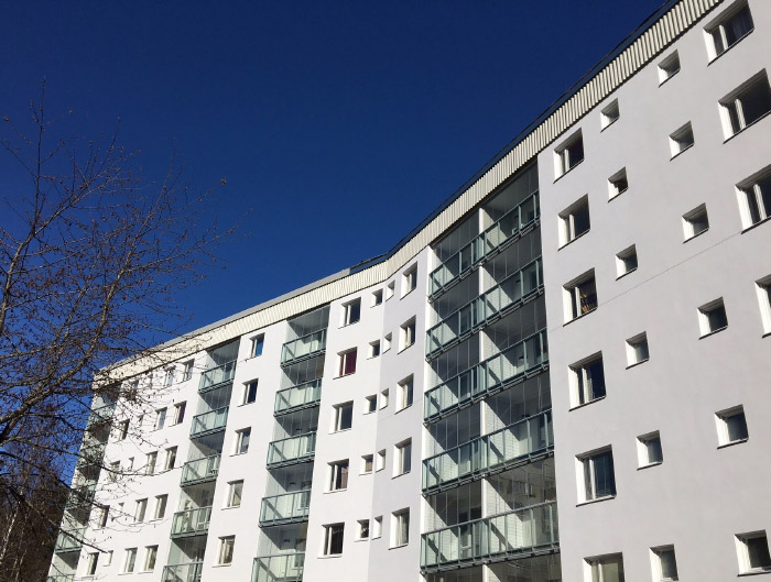 Vitt nyputsat hus med inglasade balkonger mot blå himmel.