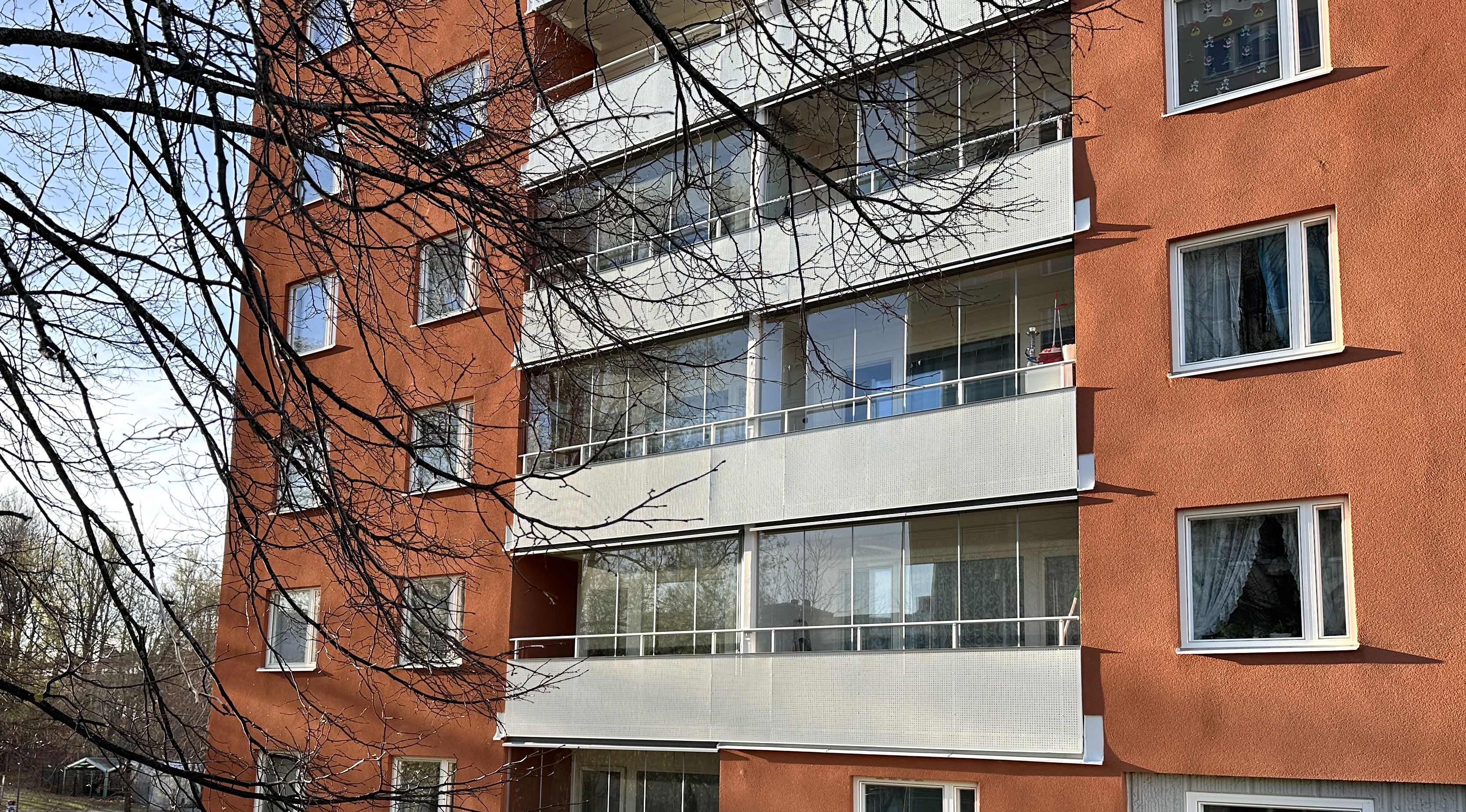 Ljusa balkonger med inglasning på hus med tegelröd puts.