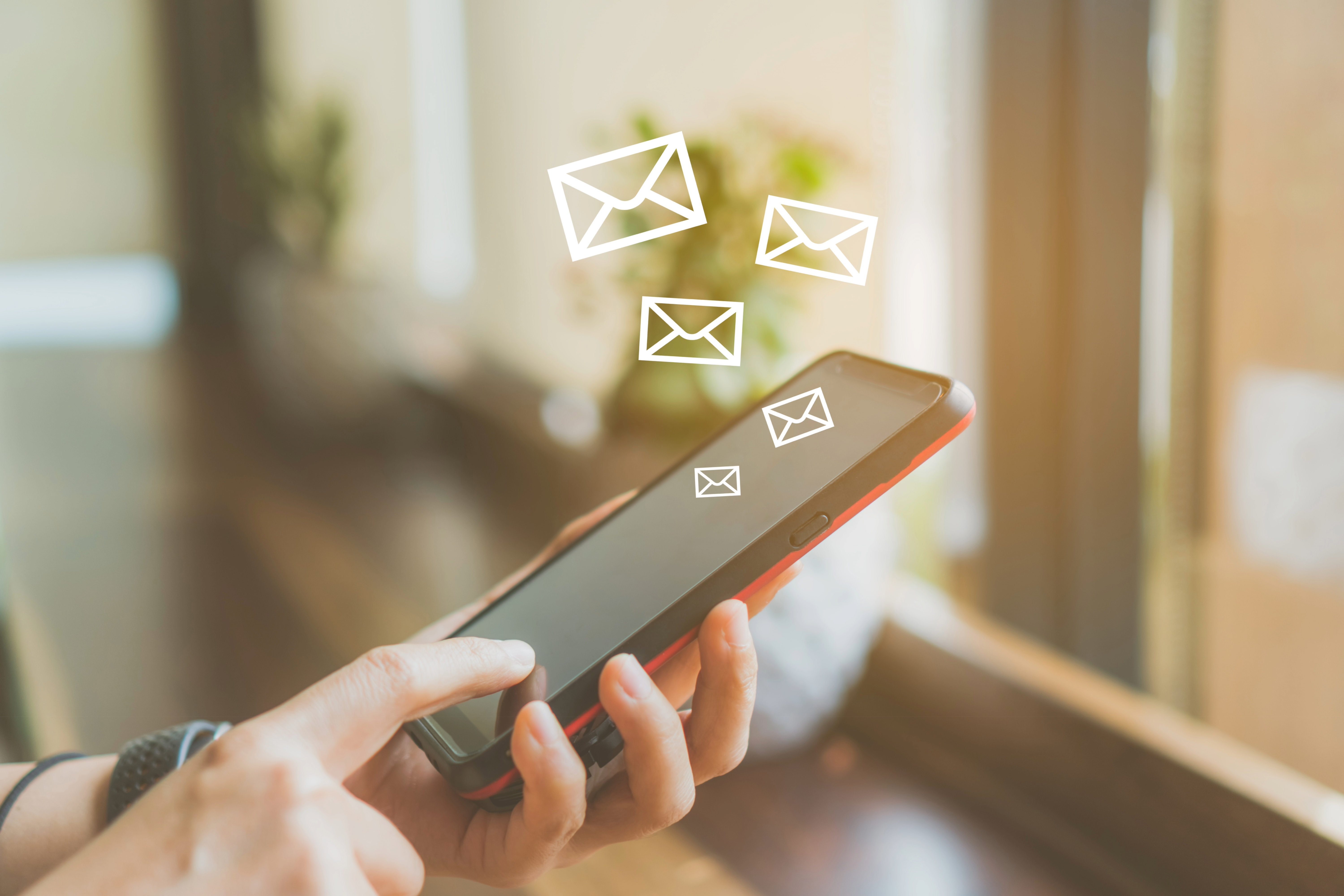 En hand håller i en smartphone och symboler av kuvert svävar ovanför.