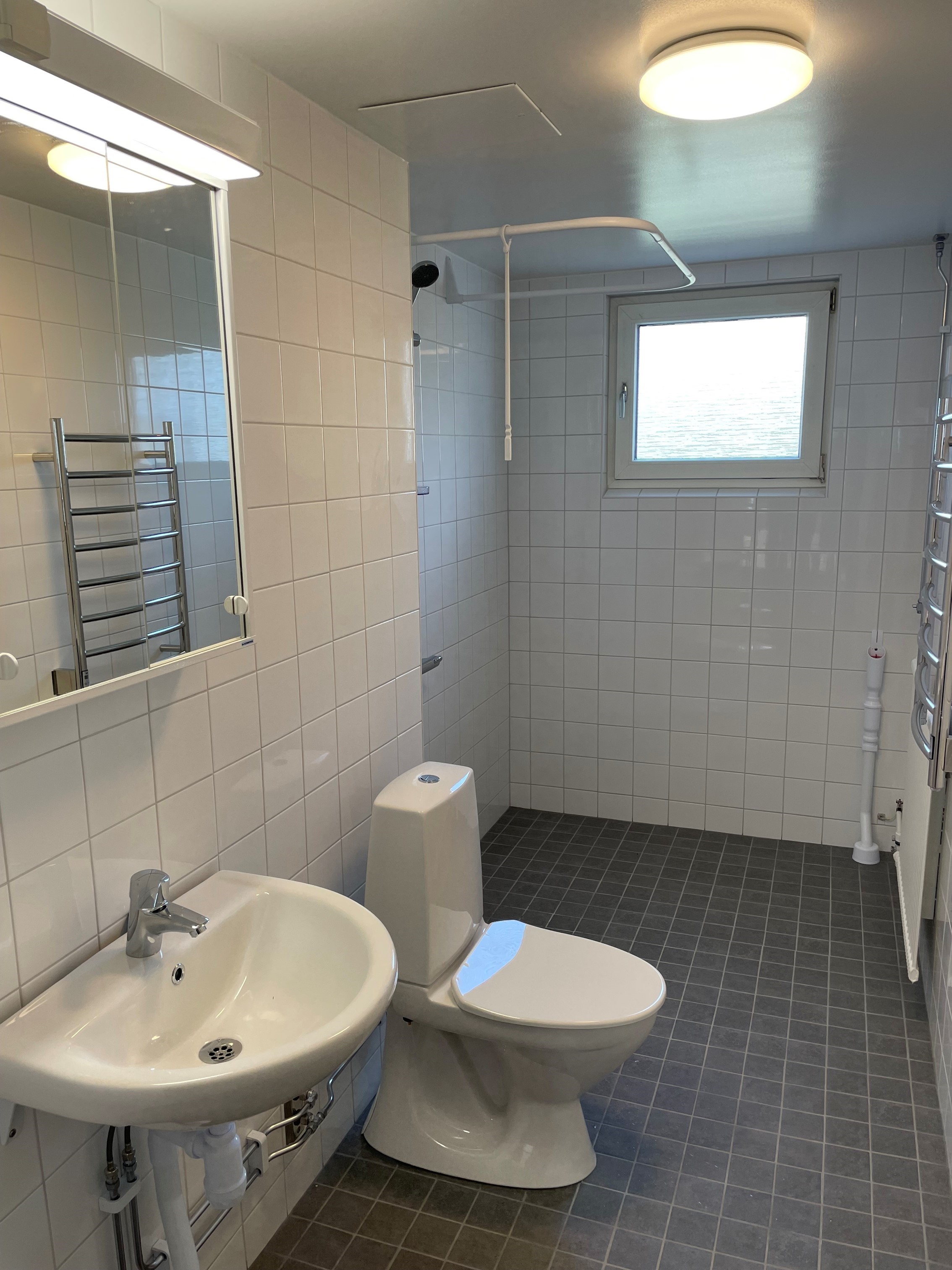 Ett badrum med vitt kakel på väggarna och grått klinker på golvet.
