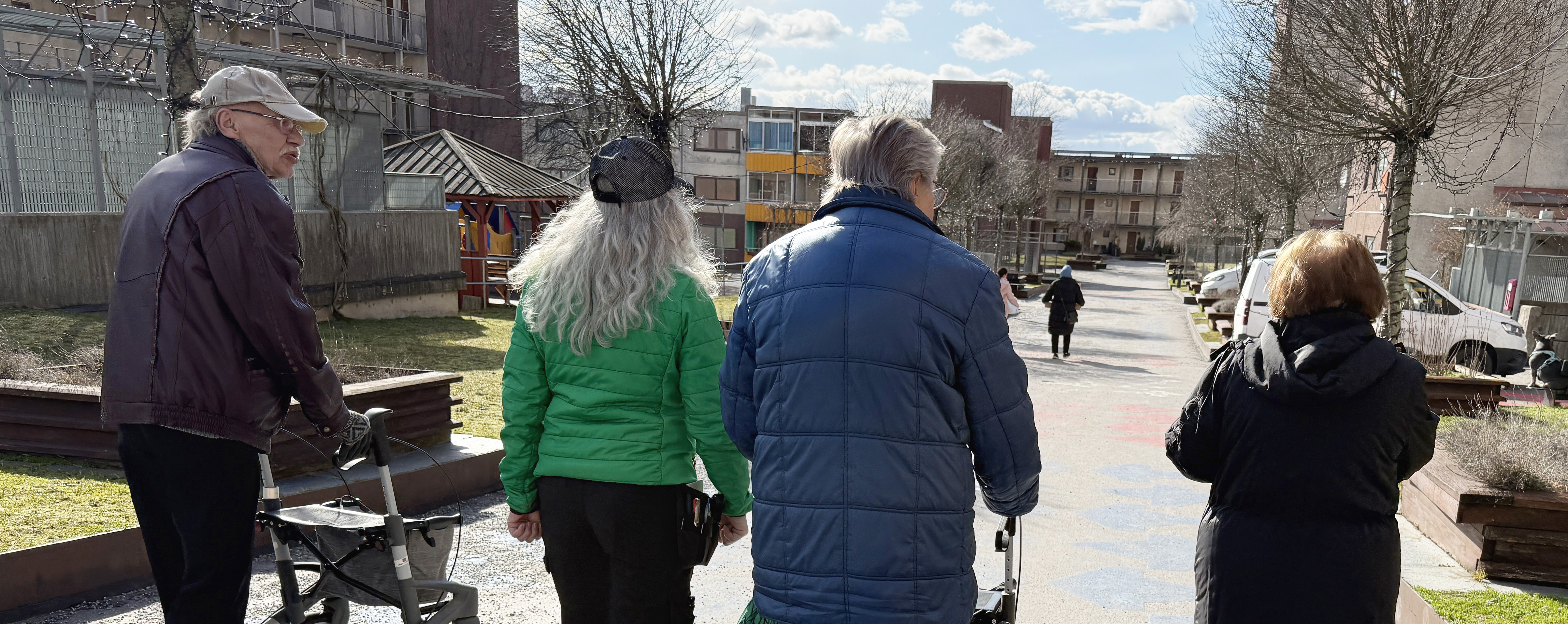 Tre personer går i ett bostadsområde en solig dag.