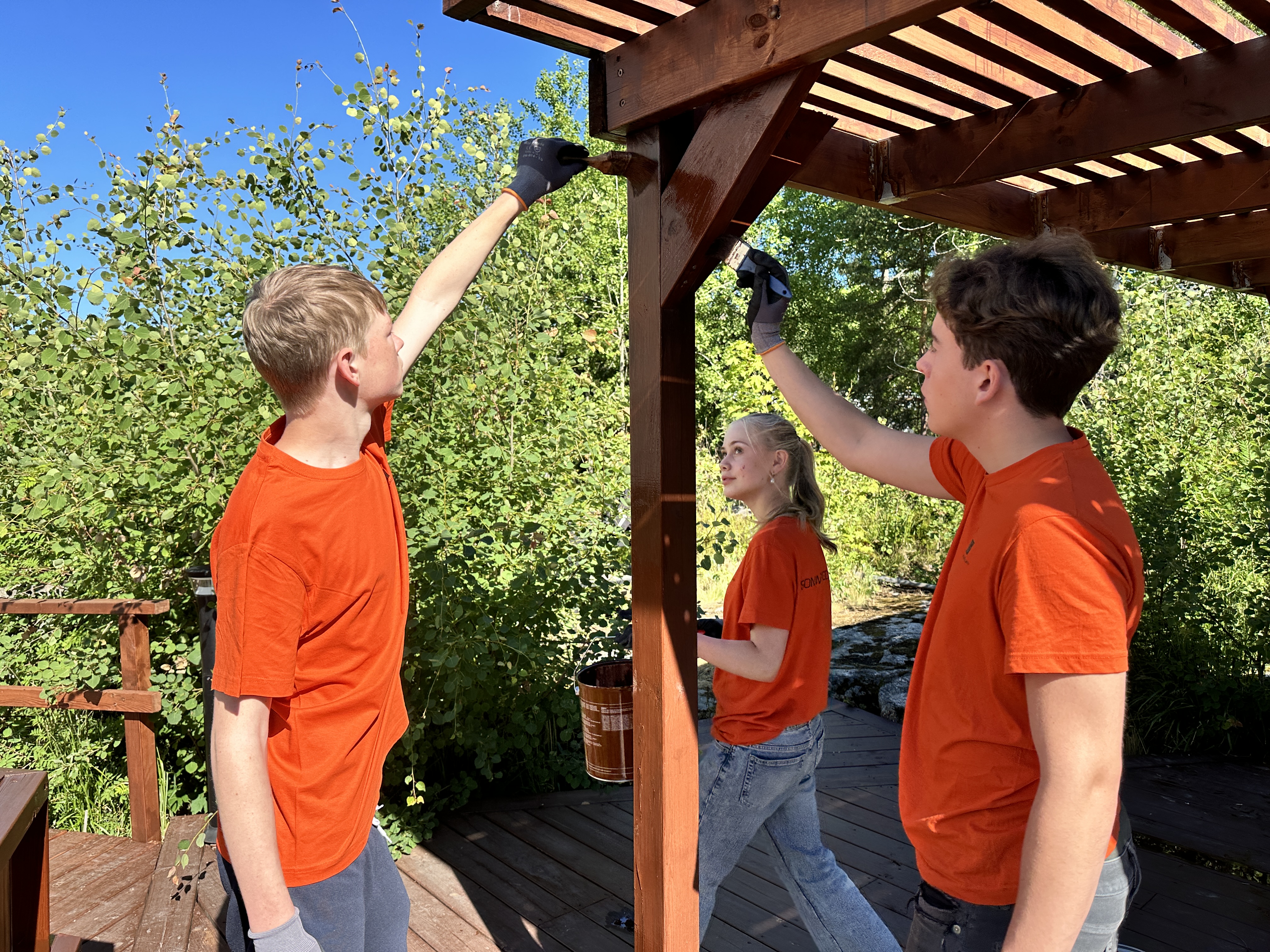 Tre ungdomare i orange t-shirt oljar in en pergola