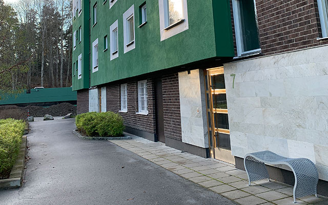 Ett flerbostadshus med grönputsad fasad och sockel av mörkbrunt tegel