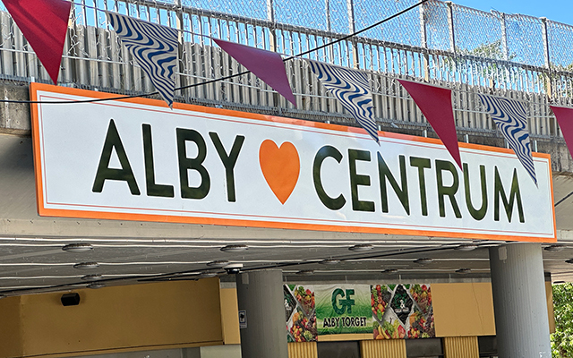 Skylt med texten Alby centrum med vimplar framför