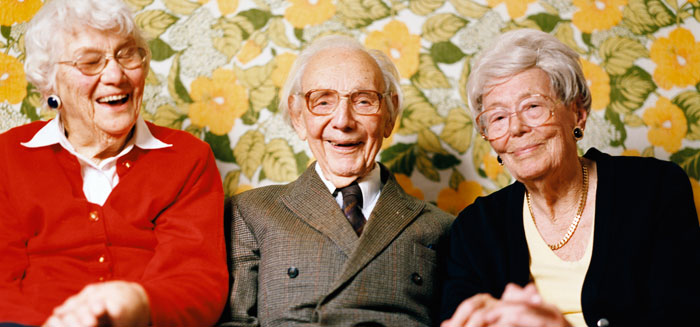 Tre glada seniorer framför en blommig tapet.