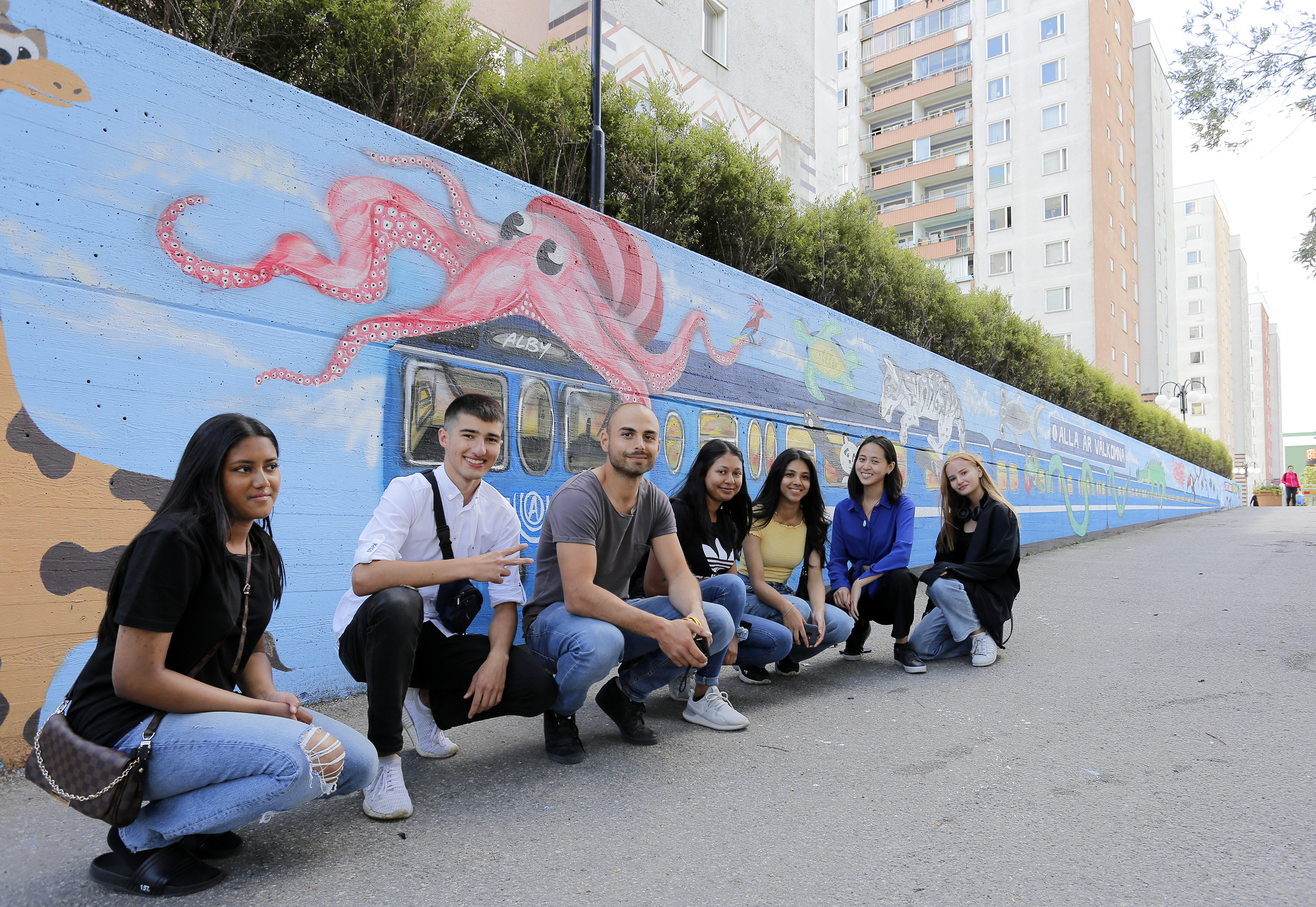 Konstnären Aris Tsartsonis hsamt sommarjobbarna Iren, Mashury, Reshma, Sofia, Aydin och Melissa framför muralmålningen i Alby.